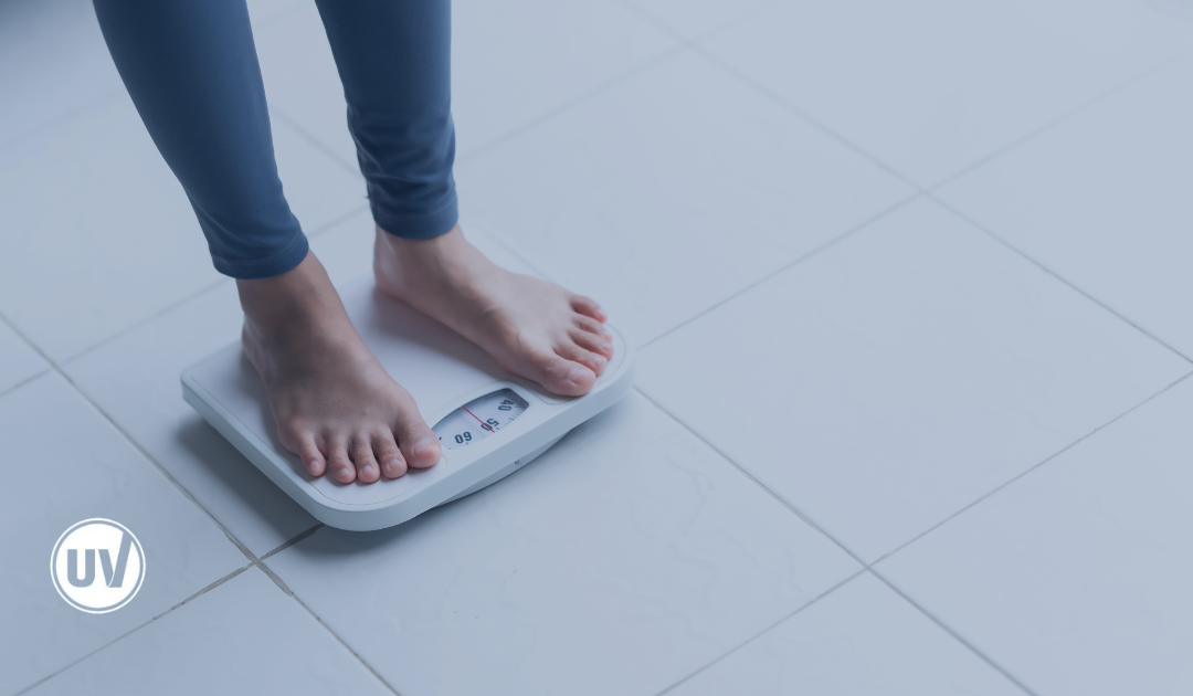 Woman stepping on a bathroom scale, monitoring her weight, illustrating weight changes related to hormonal shifts and fibroids