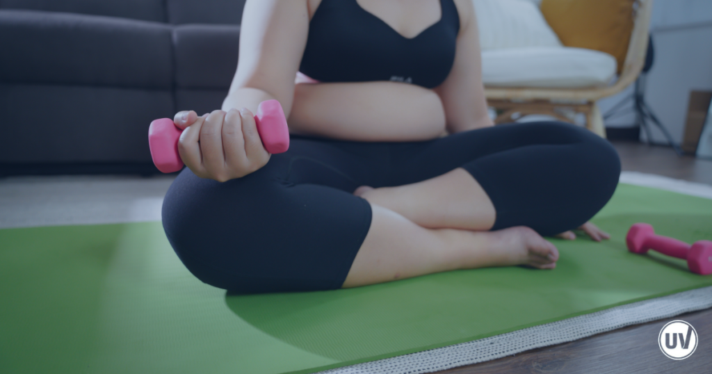 Woman on a yoga mat holding light weights, exercising indoors, representing fitness and health in relation to weight changes and hormonal shifts affecting fibroids